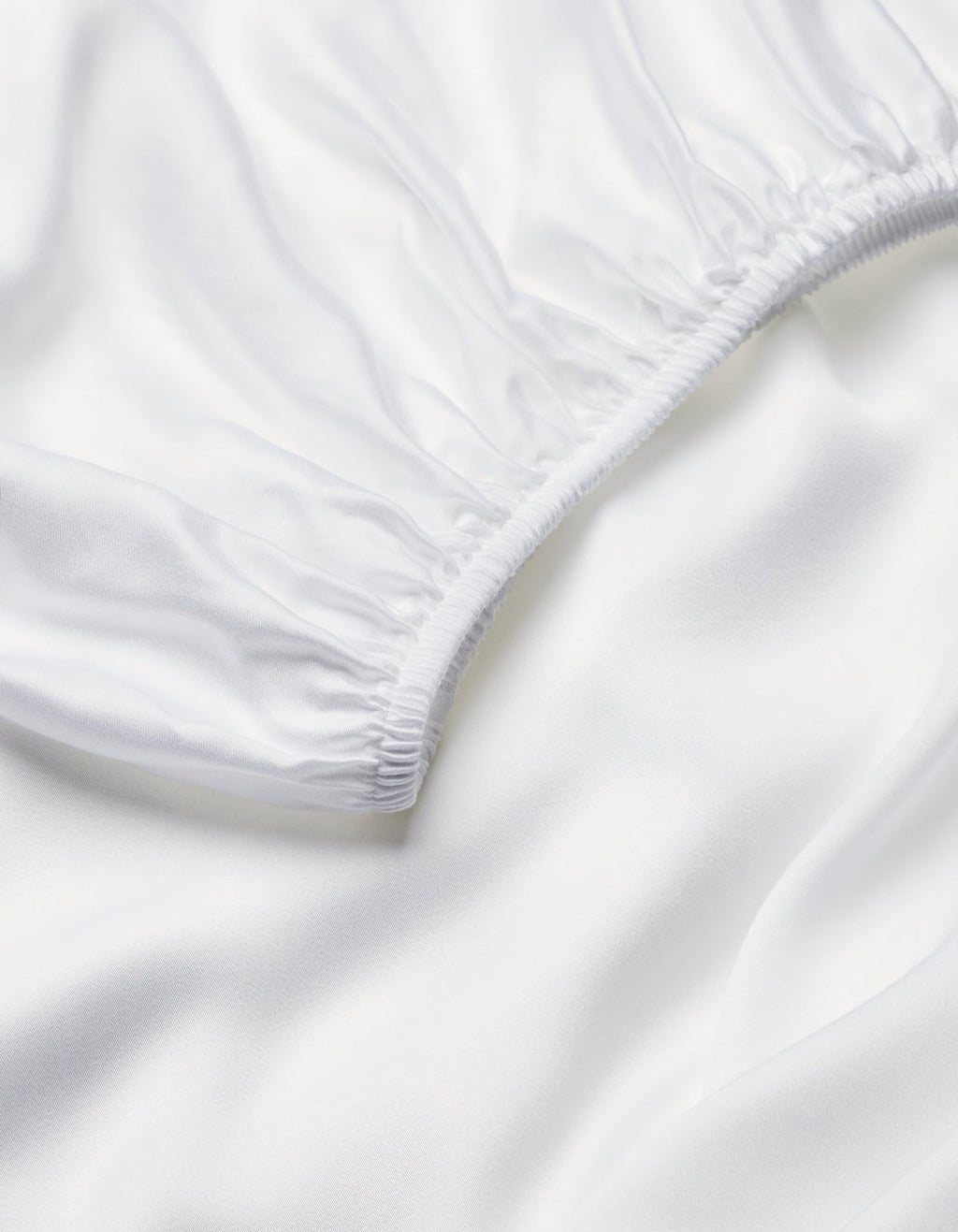 Close-up of Cozy Earth's Bamboo Fitted Sheet, featuring smooth white fabric with elastic edging and soft folds, highlighting its clean, silky texture.|Color:White