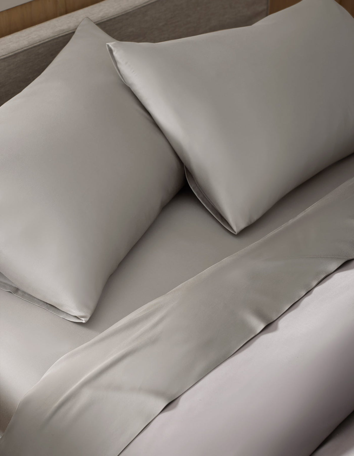 A close-up of a neatly made bed featuring the Bamboo Sheet Set by Cozy Earth in light gray, with matched pillows for a clean and elegant appearance.|Color:Light Grey