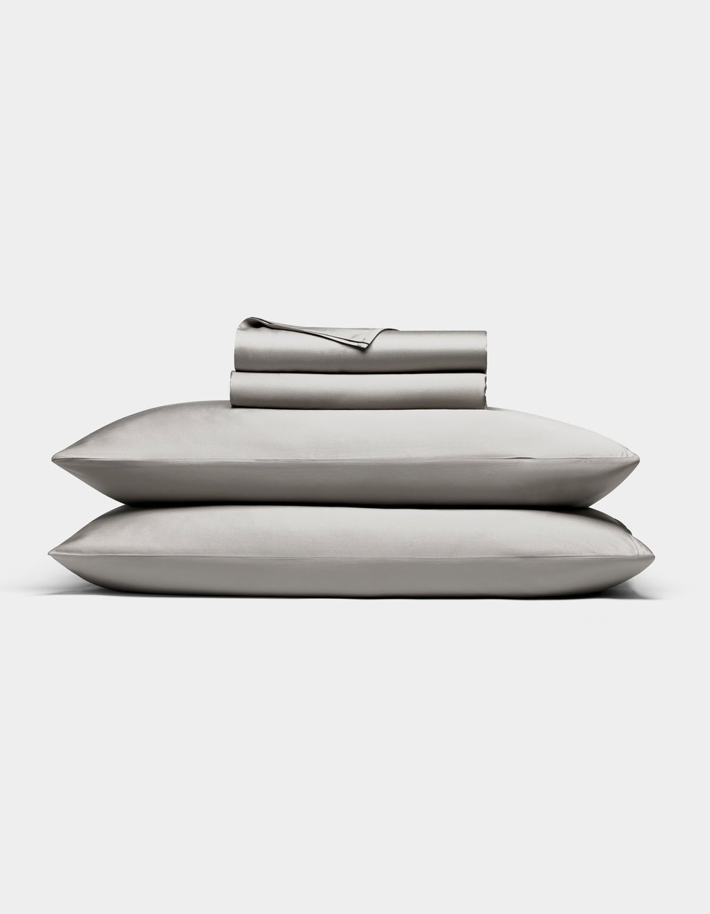 The Bamboo Sheet Set by Cozy Earth in light gray is neatly folded, with two pillows stacked and both flat and fitted sheets rolled on top, all displayed against a white background.|Color:Light Grey
