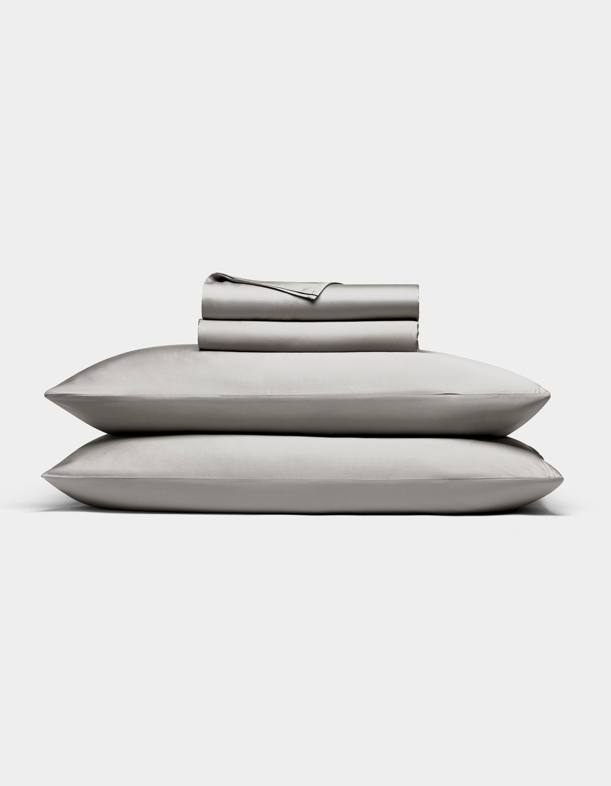 The Bamboo Sheet Set by Cozy Earth in light gray is neatly folded, with two pillows stacked and both flat and fitted sheets rolled on top, all displayed against a white background.|Color:Light Grey