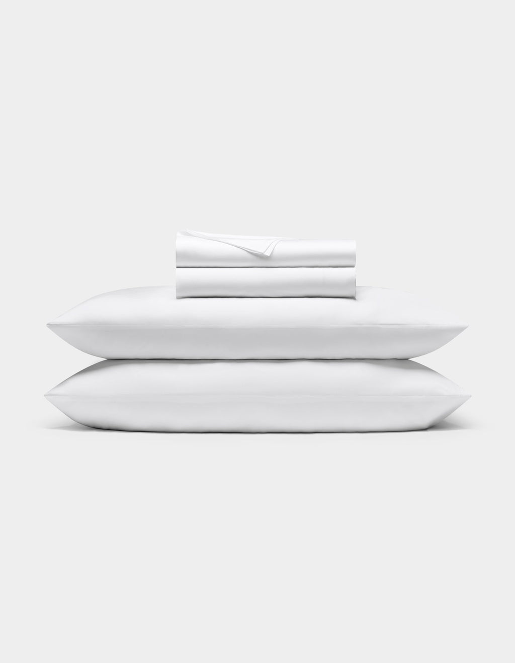 A neatly folded Bamboo Sheet Set by Cozy Earth is stacked on two white pillows, all set against a plain light gray background.|Color:White