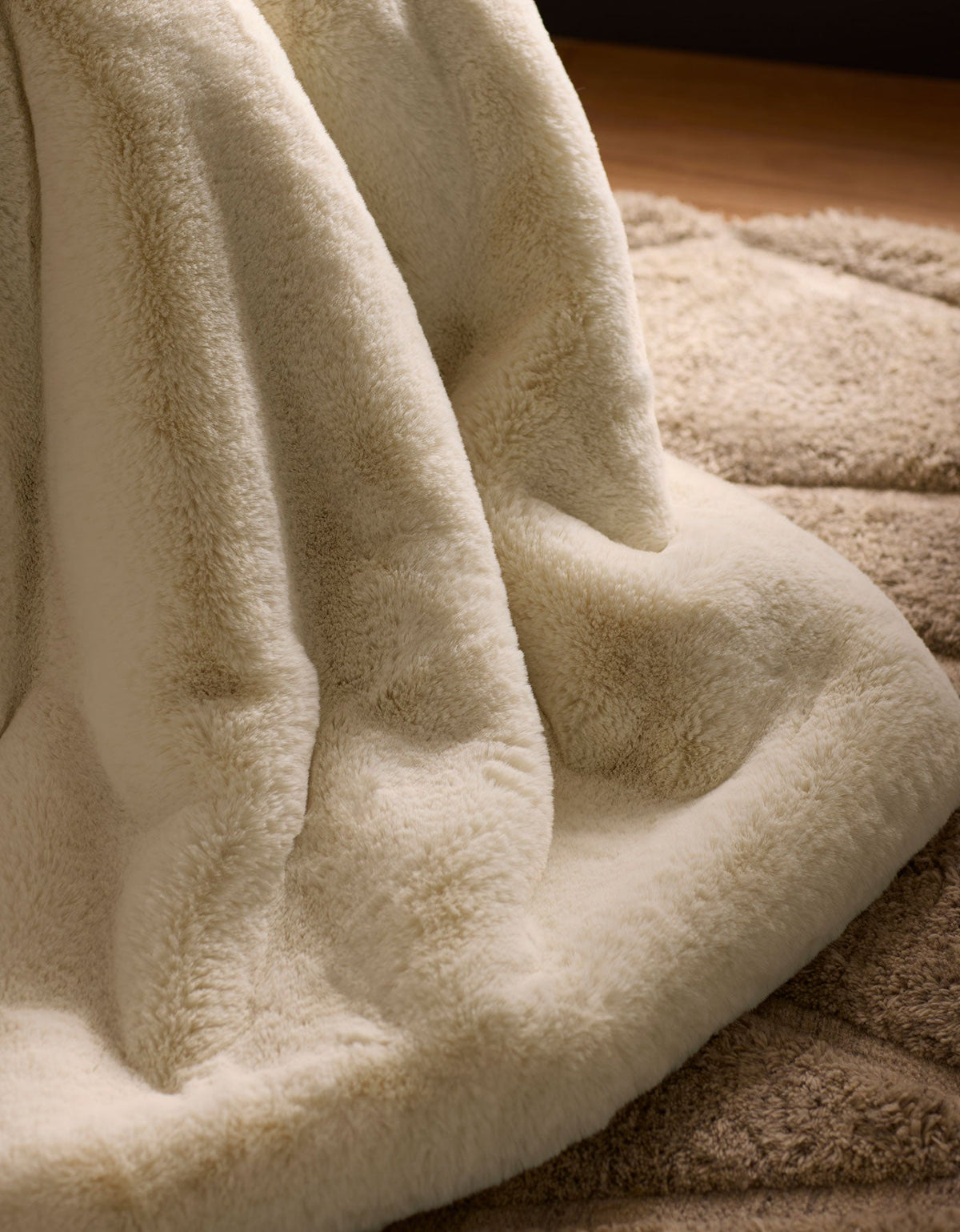 A close-up of the Cozy Earth Cuddle Blanket in cream, draped over a beige textured rug, creates a warm and cozy atmosphere.|Color:Creme
