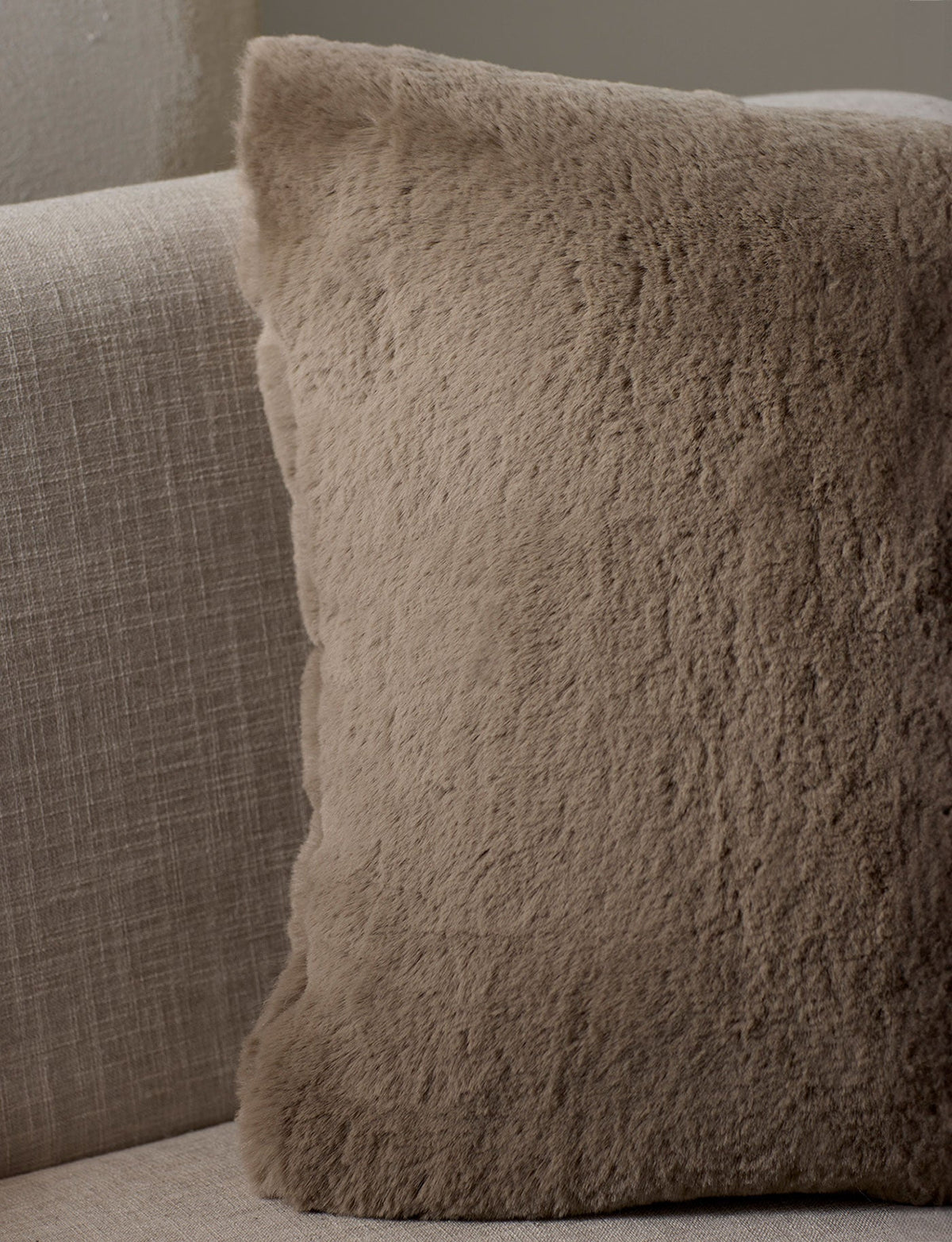 The Cozy Earth Cuddle Pillow, a square beige fuzzy throw, sits on a light fabric sofa, adding cozy softness to your neutral-toned space.|Color:Walnut |Size:20" x 20"