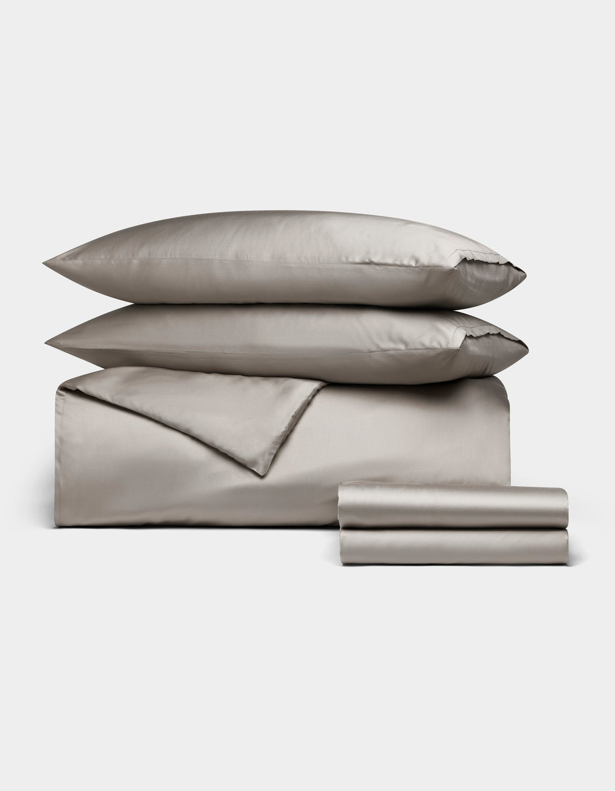 The Bamboo Bedding Deluxe Bundle by Cozy Earth features a neatly arranged silver-gray set with two pillows, a folded duvet, and stacked sheets, displayed on a plain white background.|Color:Dove Grey