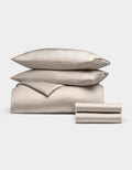 The Cozy Earth Bamboo Bedding Deluxe Bundle features two stacked pillows, a comforter, and folded sheets in cream, all neatly arranged against a plain white background.|Color:Driftwood