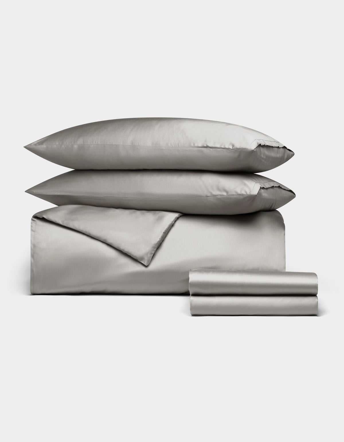 The Cozy Earth Bamboo Bedding Deluxe Bundle features light gray satin bedding with two pillows, a folded duvet, and stacked sheets, all neatly arranged on a white background.|Color:Light Grey