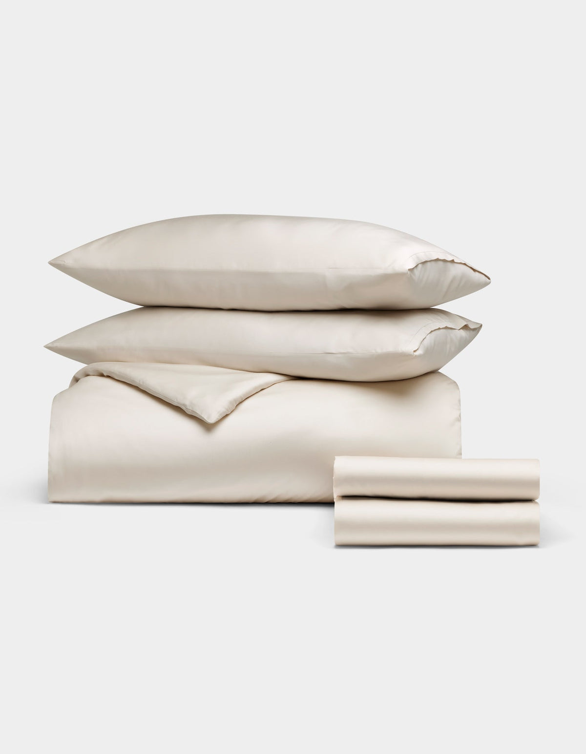 Cozy Earth's Bamboo Bedding Deluxe Bundle, featuring two pillows, a folded comforter, and two folded sheets in cream, is neatly stacked and displayed on a plain white background.|Color:Oat