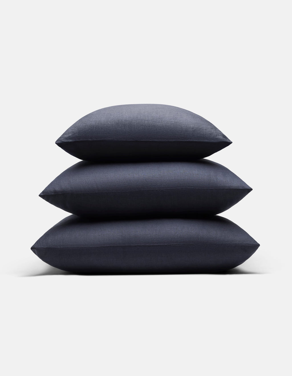 Three Cozy Earth Linen Throw Pillows in dark blue are stacked neatly on top of each other against a plain white background.|Color:Eclipse|Size:24" x 24"