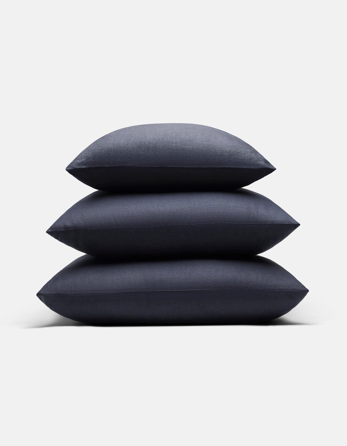 Three Cozy Earth Linen Throw Pillows in dark blue are stacked neatly on top of each other against a plain white background.|Color:Eclipse|Size:24" x 24"