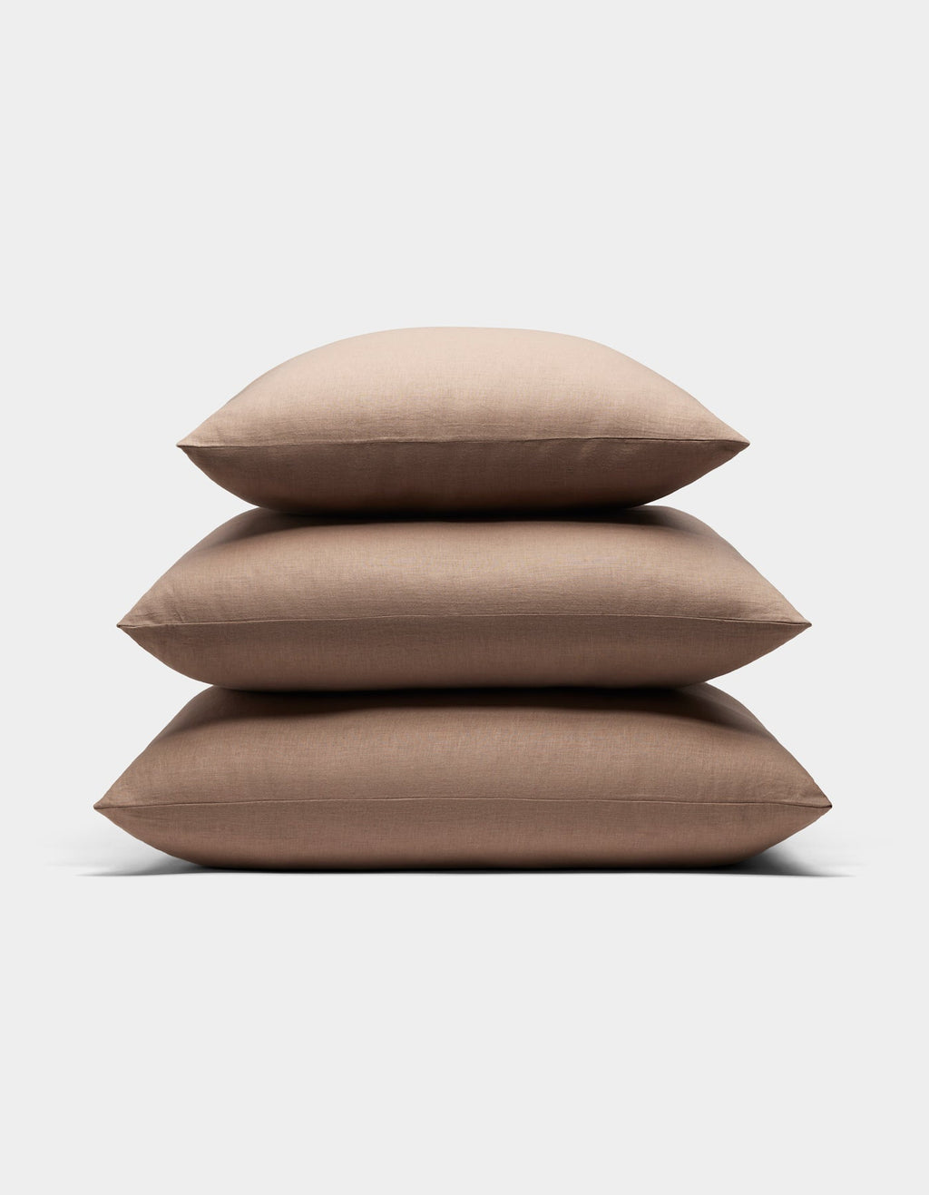Three Cozy Earth Linen Throw Pillows in light brown are stacked neatly on top of each other against a plain white background.|Color:Maple|Size:20" x 20"