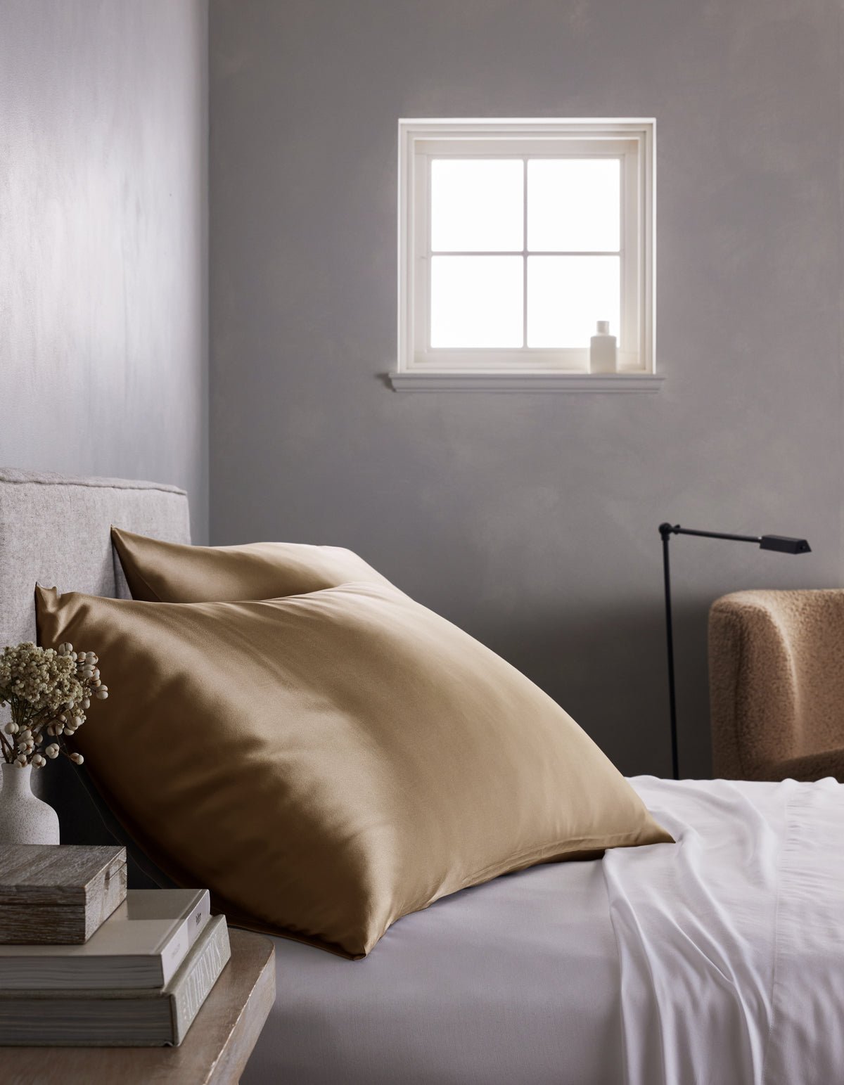A neatly made bed features a Cozy Earth Silk Pillowcase, crisp white sheets, and a stack of books on the bedside table, all set against a gray wall with soft natural light streaming in through the window.|Color:Walnut