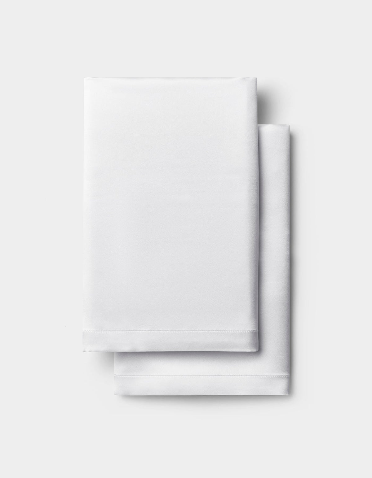 A neatly folded white Silk Pillowcase by Cozy Earth is stacked on a light gray background.|Color:White
