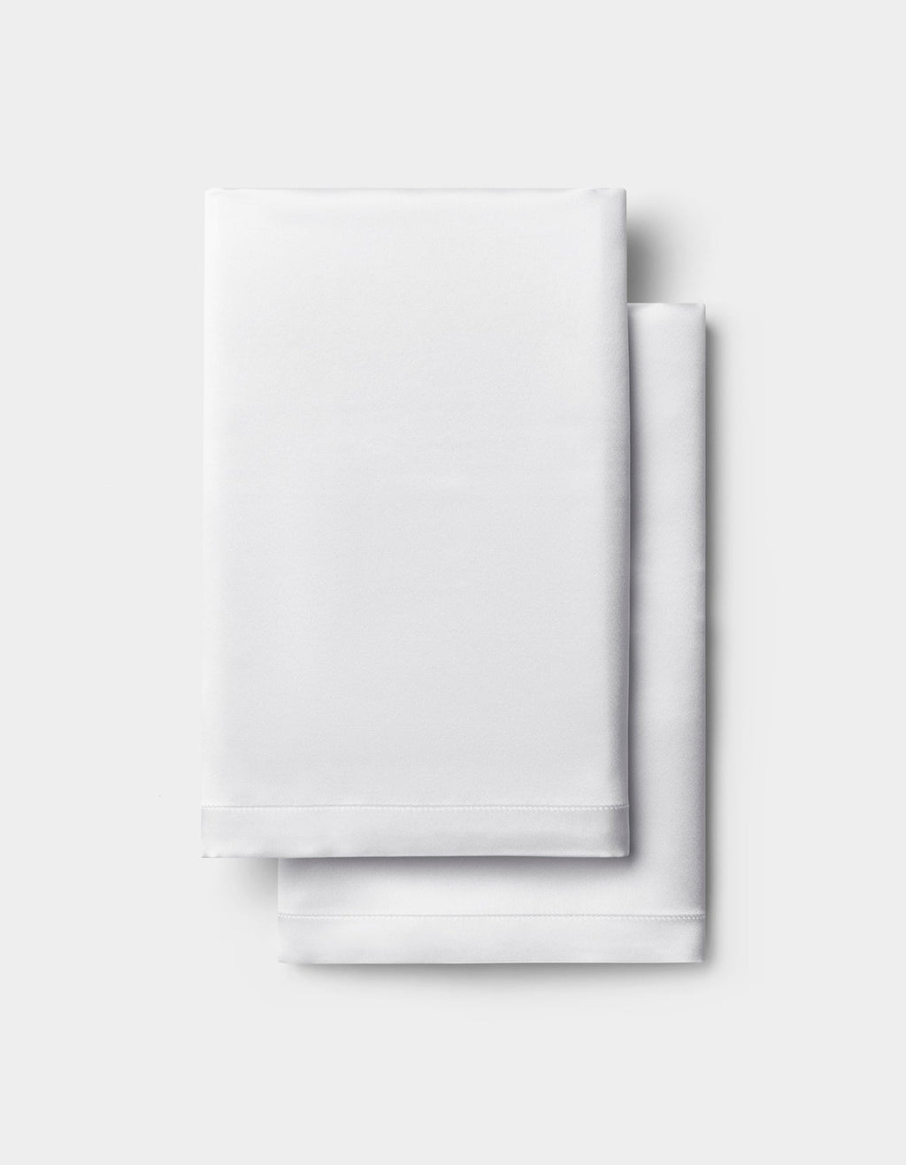 A neatly folded white Silk Pillowcase by Cozy Earth is stacked on a light gray background.|Color:White