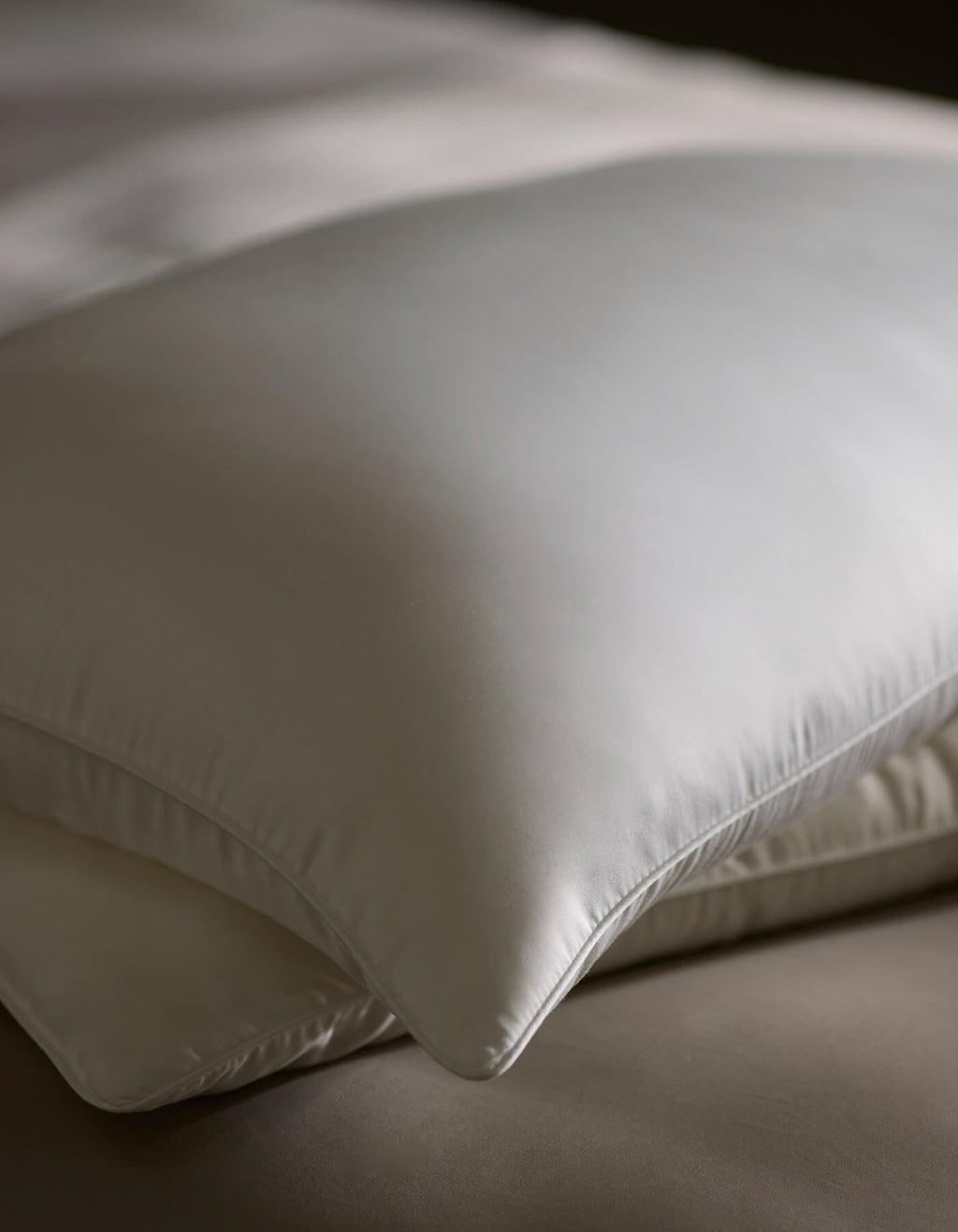 A close-up of Cozy Earth's Silk Insert Bundle—two stacked, silky white pillows—rests on a neatly made bed under soft lighting.|Filling:Standard