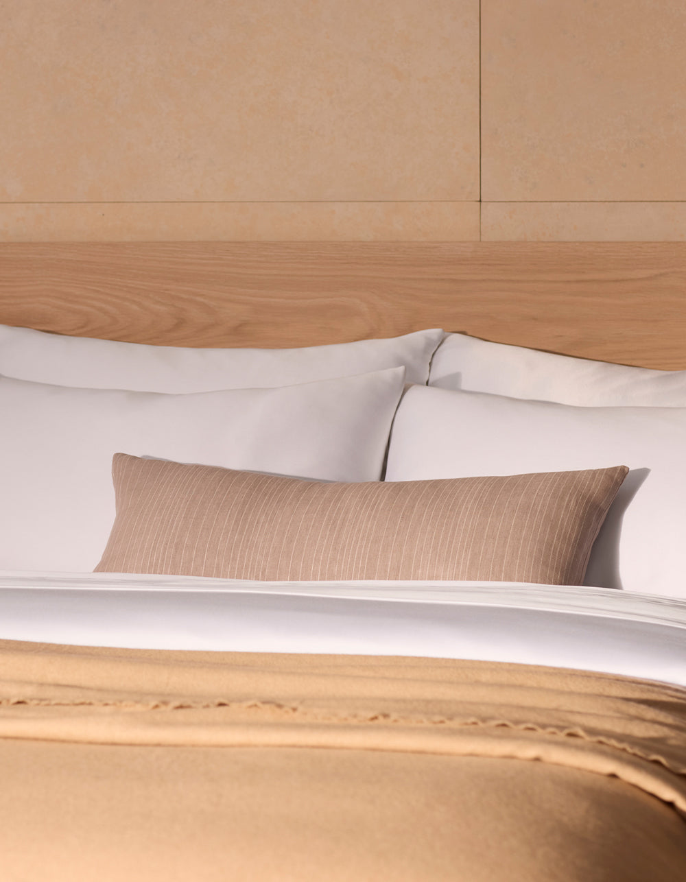 A neatly made bed with white pillows, a Cozy Earth Striped Throw Pillow, a light wooden headboard, and a beige blanket folded at the foot of the bed.|Color:Clay|Size:14" x 30"