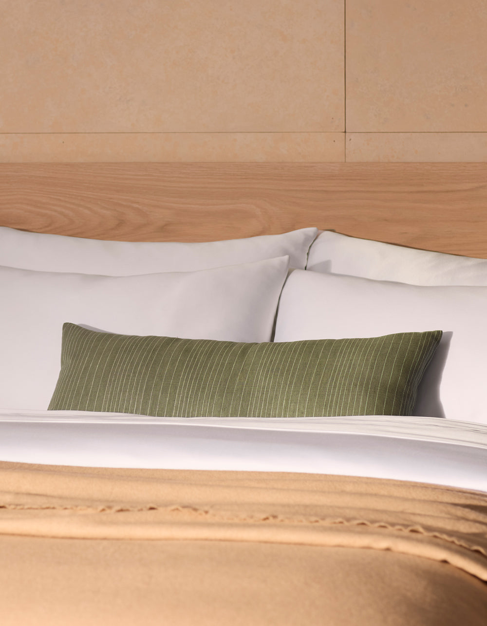 A neatly made bed with white linens and pillows, a Cozy Earth Striped Throw Pillow as an accent, and a beige blanket at the foot, set against a light wood headboard and tan wall.|Color:Smoke|Size:14" x 30"