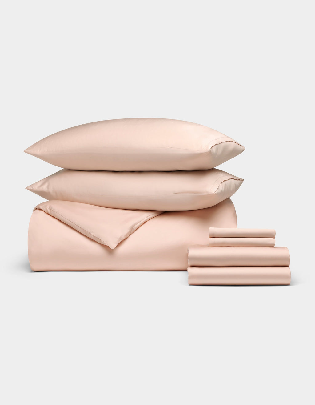 The Bamboo Bedding Ultimate Bundle by Cozy Earth, in light peach, features two stacked pillows, a folded comforter, and neatly folded sheets displayed on a plain light background.|Color:Peony