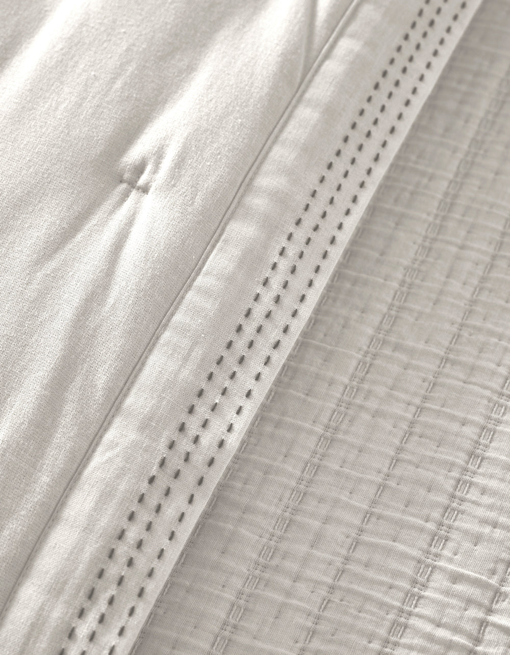 Close-up of the Cozy Earth Baja Quilt in white, featuring quilted stitching and a decorative perforated hem that highlights the soft, textured woven details.|Color:Laurel Stripe/Striped Bone