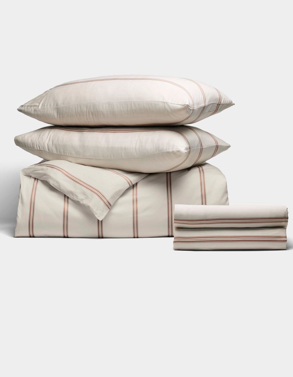 The Cozy Earth Bamboo Bedding Deluxe Bundle features a neatly stacked set with thin red and gray stripes on a cream background, including two large pillows, a folded comforter, and two sheets, displayed against a light backdrop.|Color:Baja Stripe in Maple