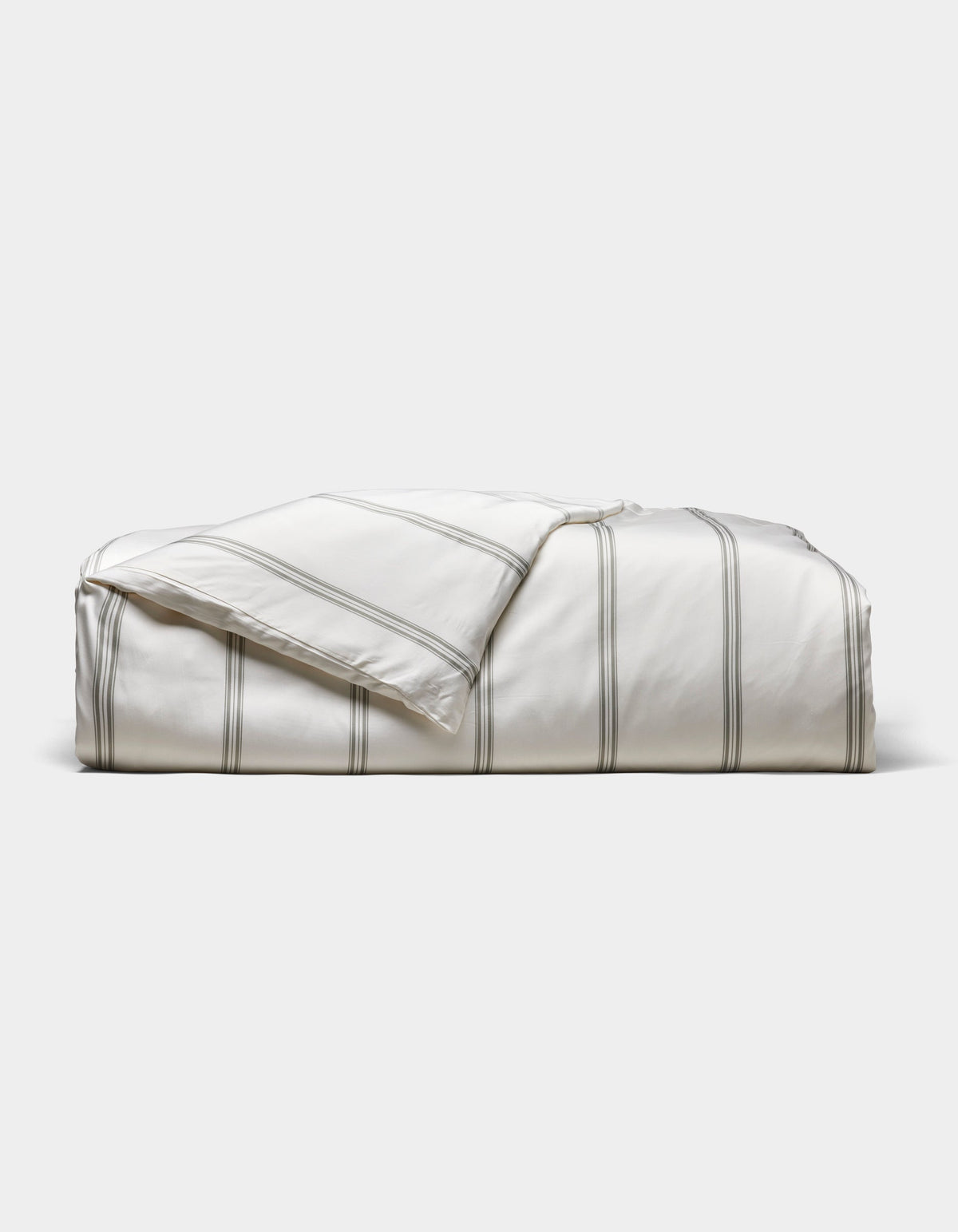 The Cozy Earth Bamboo Duvet Cover, white with thin gray stripes, is neatly folded against a light gray background. A corner is turned down to reveal the underside.|Color:Baja Stripe in Laurel