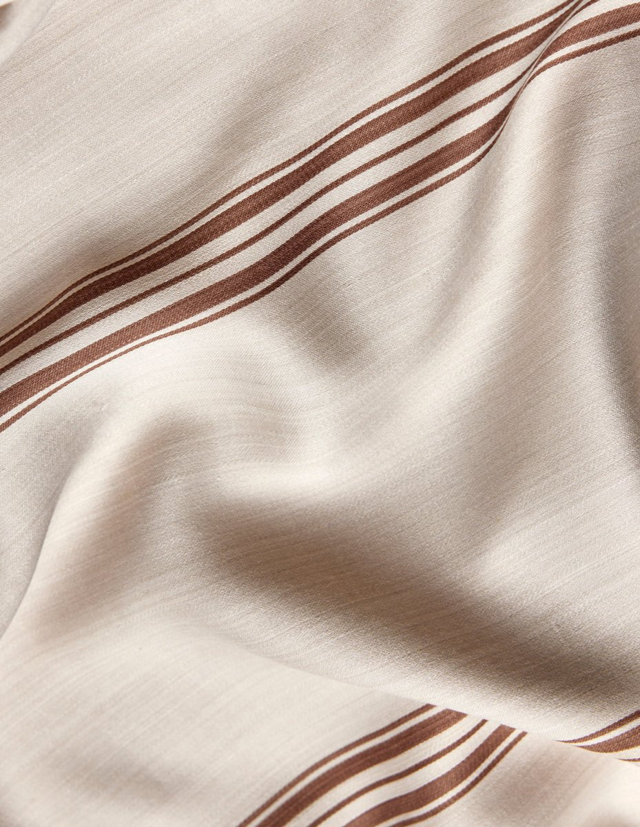 A close-up of Cozy Earth's Bamboo Sheet Set in beige, featuring brown parallel stripes, gentle folds, and a smooth, slightly shiny finish.|Color:Baja Stripe in Maple
