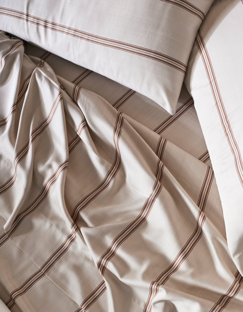 Cozy Earth's Bamboo Pillowcases in beige, featuring brown horizontal stripes, are shown slightly rumpled and overlapping for a casual, inviting vibe.|Color:Baja Stripe in Maple