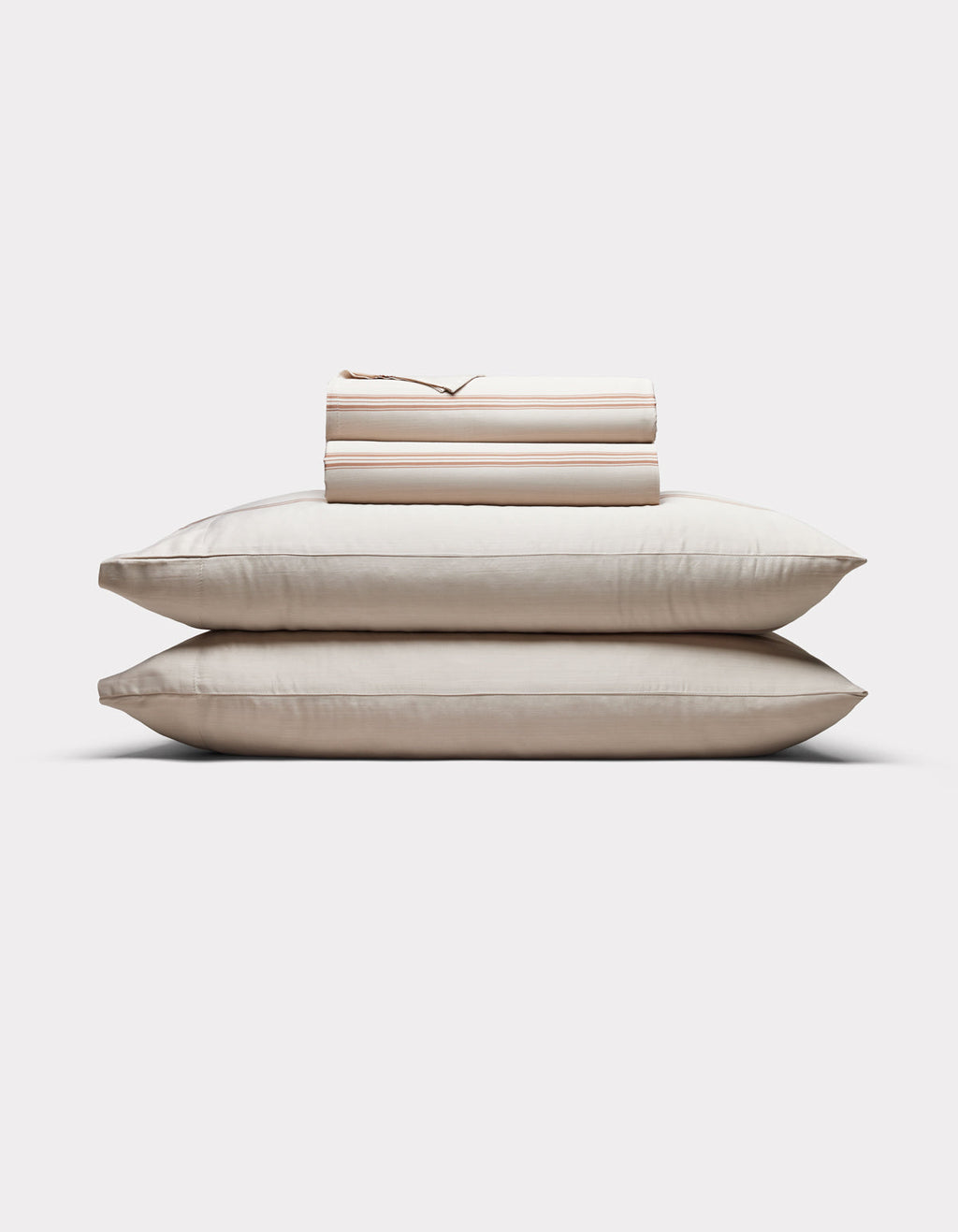 Two cream-colored pillows are stacked with Cozy Earth’s Bamboo Sheet Set, neatly folded on top, all arranged against a plain white background.|Color:Baja Stripe in Maple