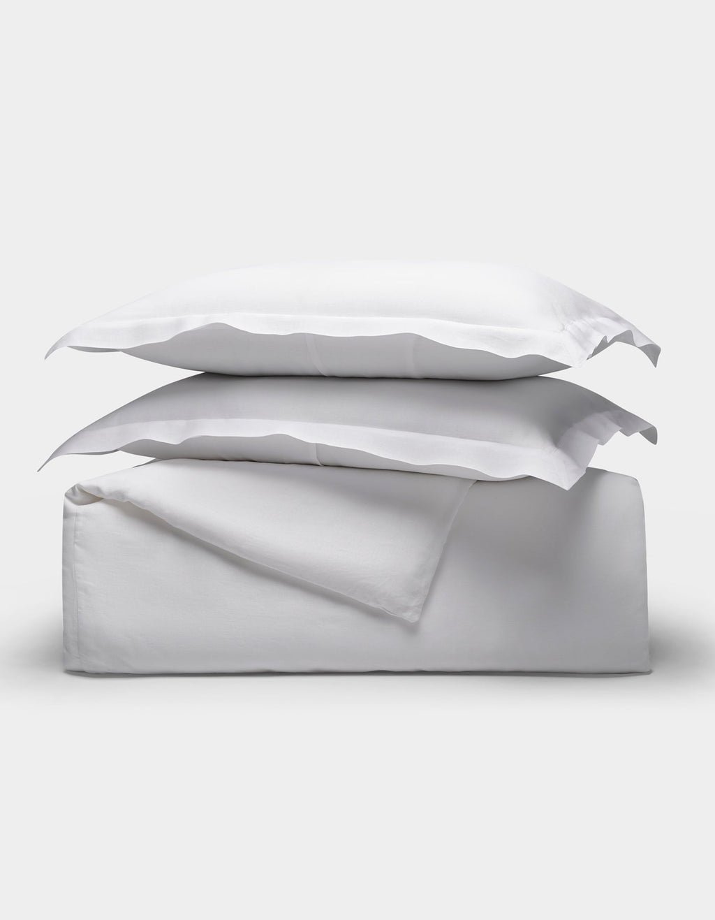 The Linen Duvet Set by Cozy Earth is shown neatly folded with two stacked pillows, arranged on top of folded sheets against a plain light background.|Color:White