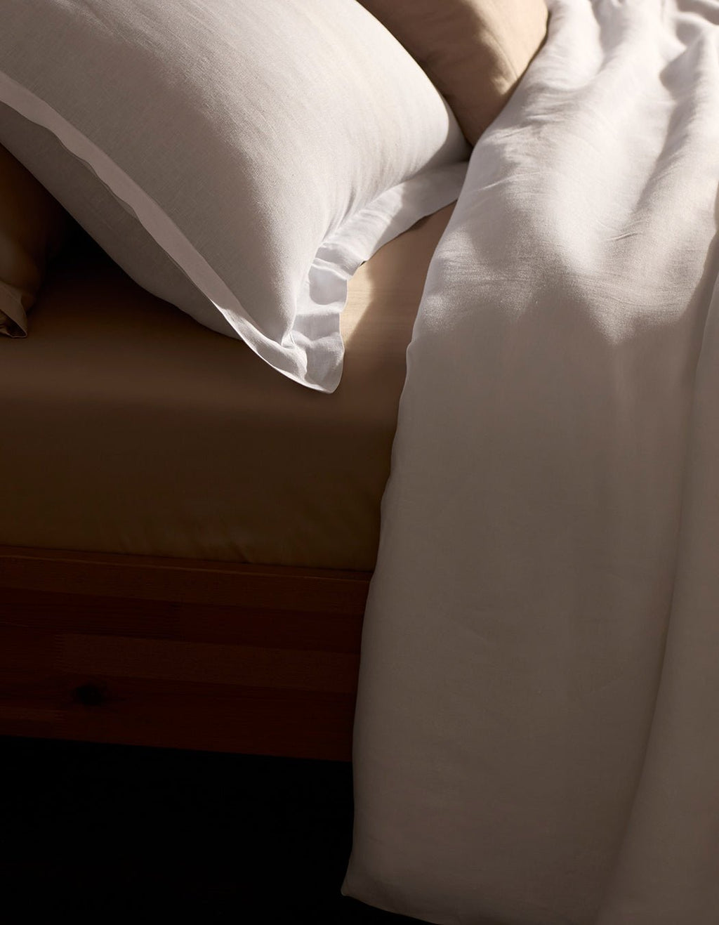 A close-up of a neatly made bed features the Cozy Earth Linen Duvet Set in beige, paired with a white bordered pillow and white blanket, all elegantly draped over a wooden bed frame.|Color:White