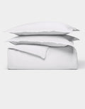 The Cozy Earth Soft-Wash Cotton Duvet Bundle features a neatly folded white sheet set with two stacked pillows, all displayed against a plain white background.|Color:White