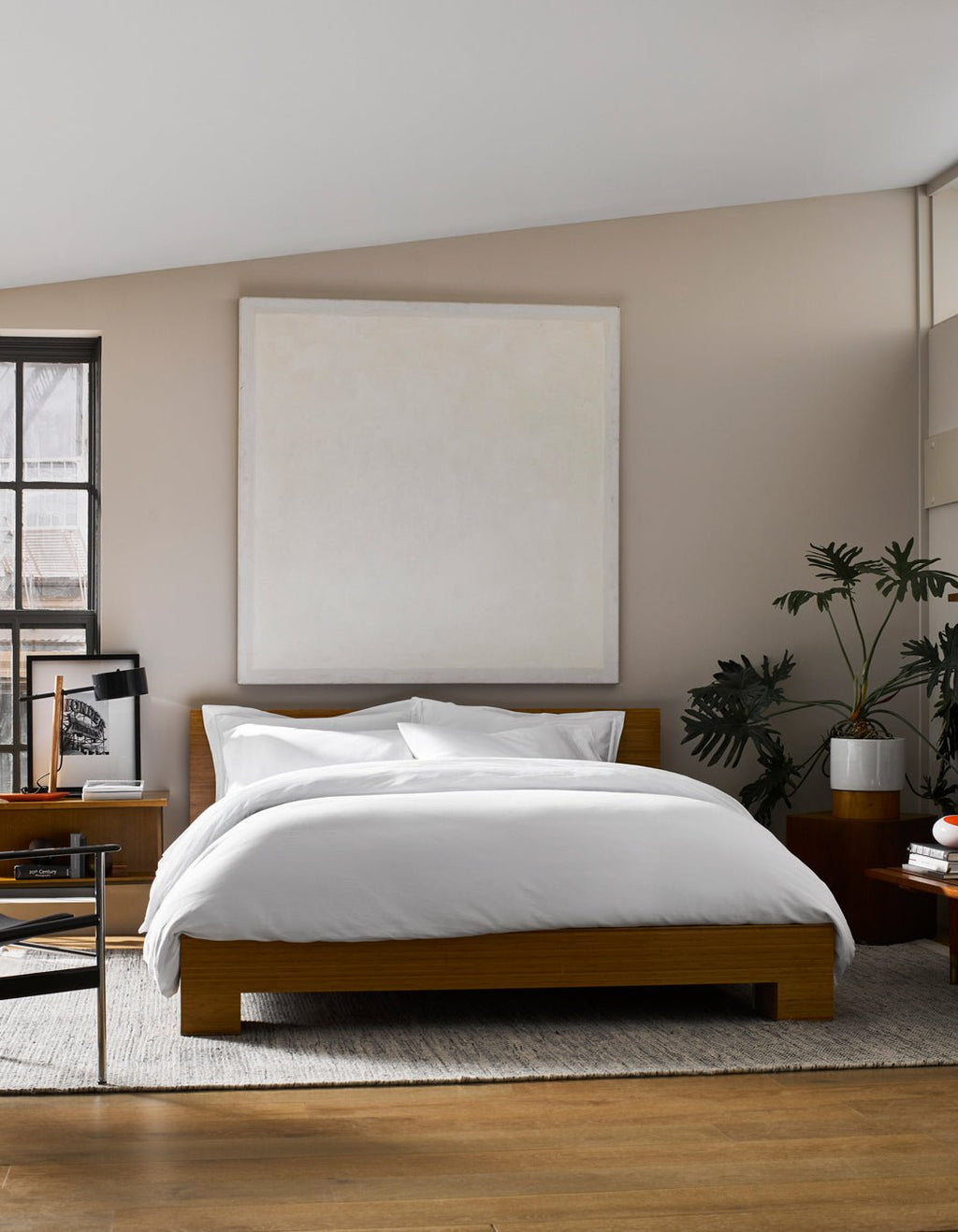A modern bedroom featuring a wooden bed frame, Cozy Earth Soft-Wash Cotton Duvet Cover in white, a large blank square canvas above the bed, gray area rug, potted plant, and natural light streaming from the left window.|Color:White
