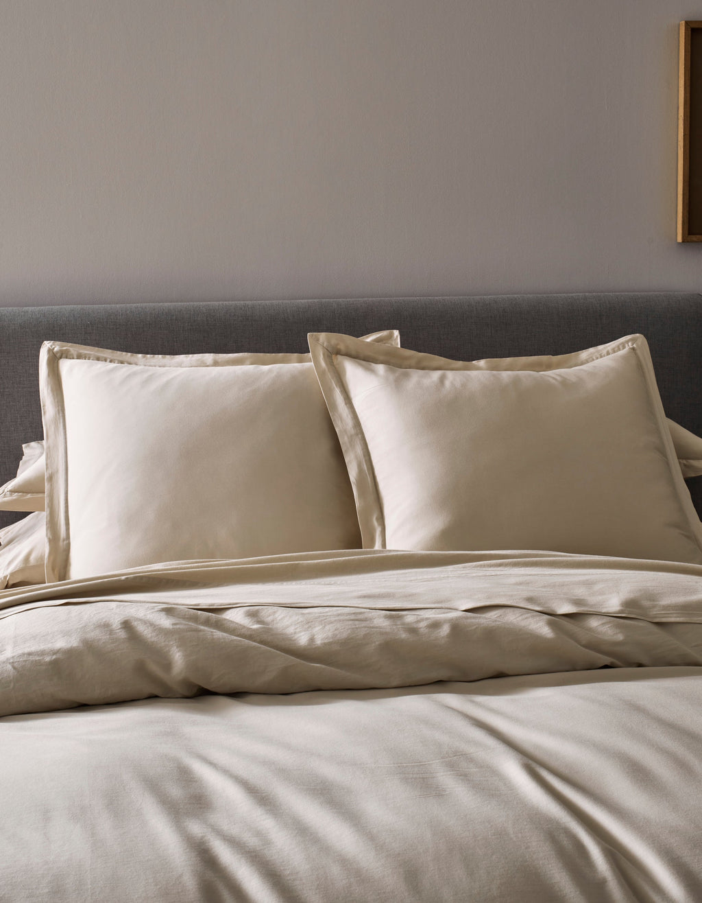 Two Soft-Wash Cotton Shams by Cozy Earth in beige rest against a gray upholstered headboard, paired with a coordinated beige comforter and sheets, creating a neat, minimal look in this modern bedroom.|Color:Driftwood