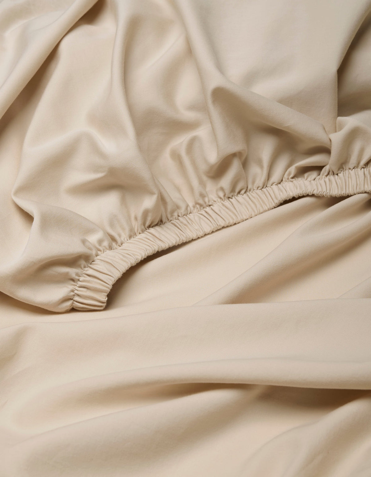 Close-up of beige Soft-Wash Cotton Fitted Sheet by Cozy Earth, featuring smooth fabric with an elastic seam and gathered details.|Color:Driftwood