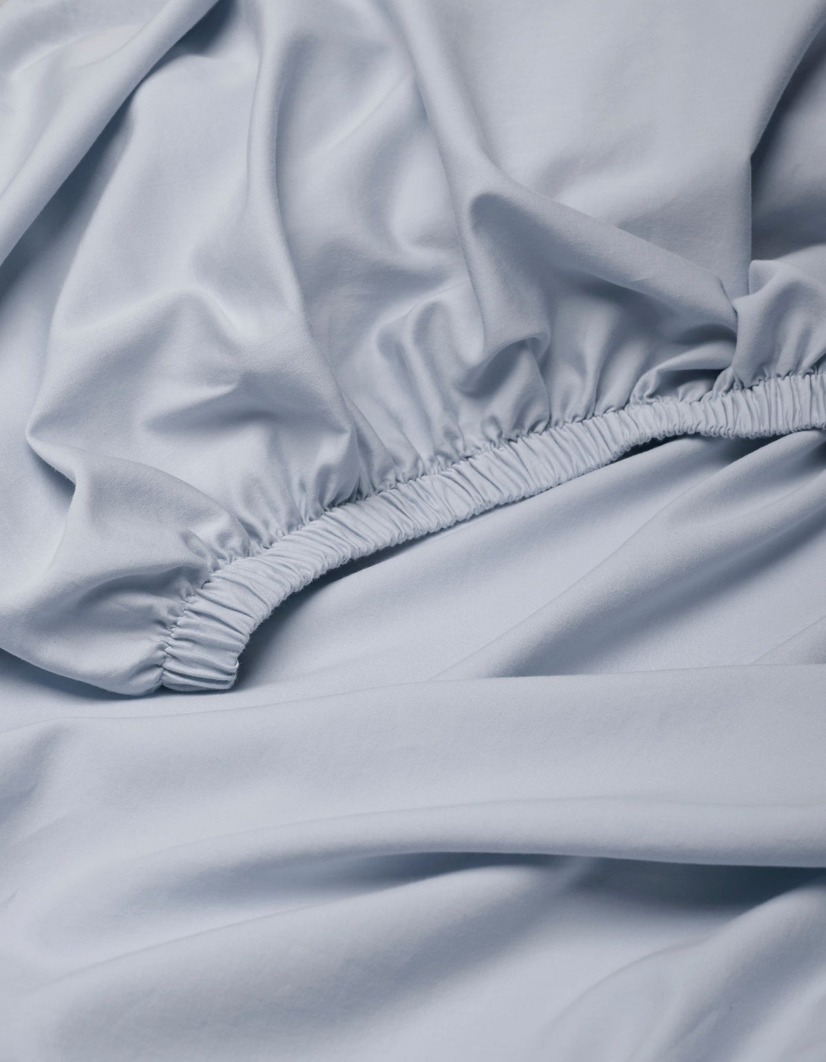 The Cozy Earth Soft-Wash Cotton Fitted Sheet features a light blue color, gathered elastic edge, and close-up view highlighting its smooth texture and soft folds.|Color:Shore