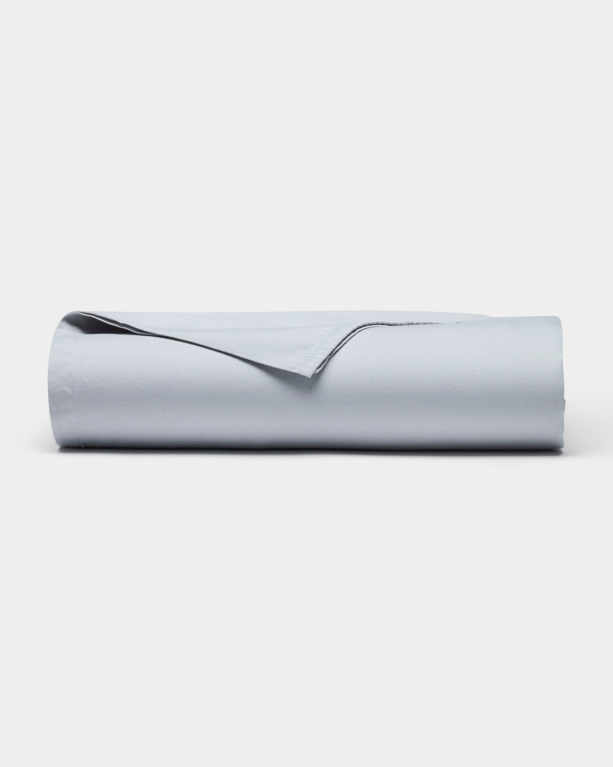 The Soft-Wash Cotton Sheet Set by Cozy Earth is shown neatly rolled up in light gray on a plain white background, with one corner gently lifted.|Color:Shore
