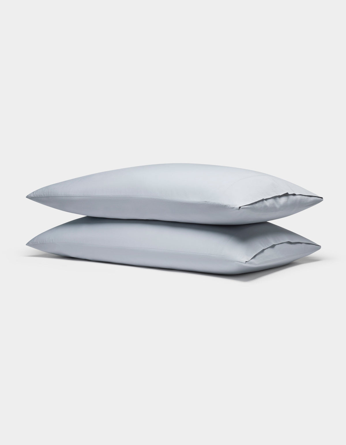 Two Soft-Wash Cotton Pillowcases by Cozy Earth, in light gray, are neatly stacked against a plain white background.|Color:Shore