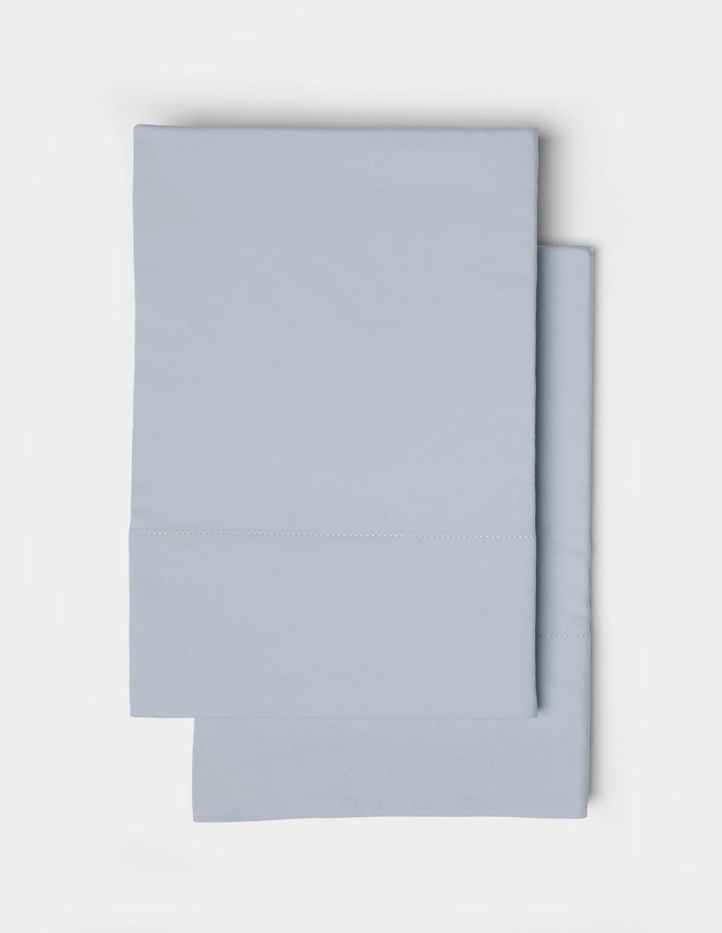 Two neatly folded Soft-Wash Cotton Pillowcases by Cozy Earth, in light blue, are stacked on top of each other against a white background.|Color:Shore