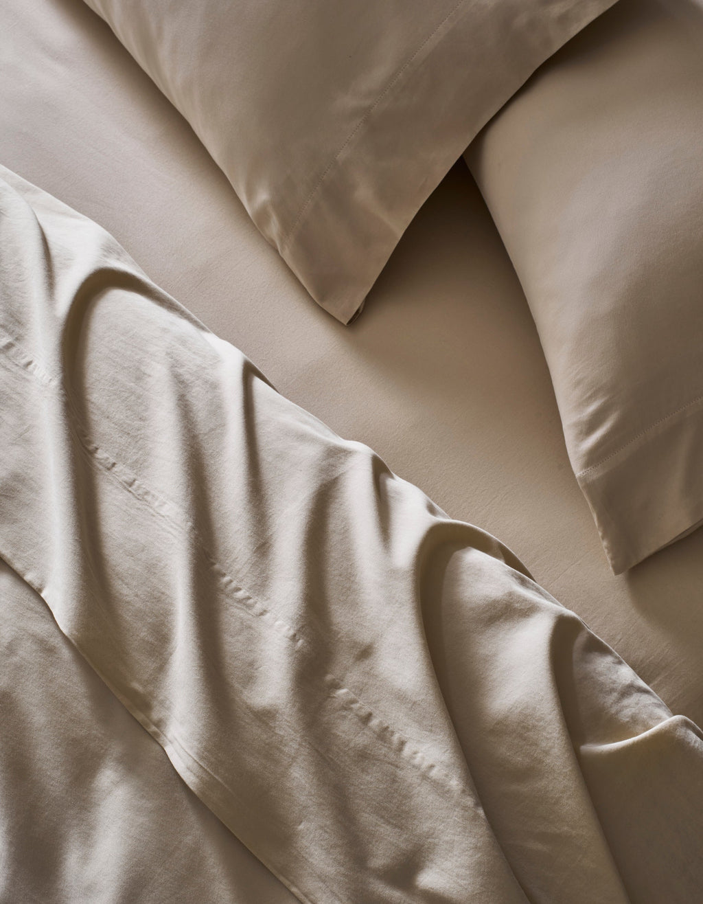 A close-up of a bed made with Cozy Earth’s Soft-Wash Cotton Bedding Deluxe Bundle – Down Alternative shows smooth beige sheets and pillowcases, giving the room a calm and inviting vibe.|Color:Driftwood