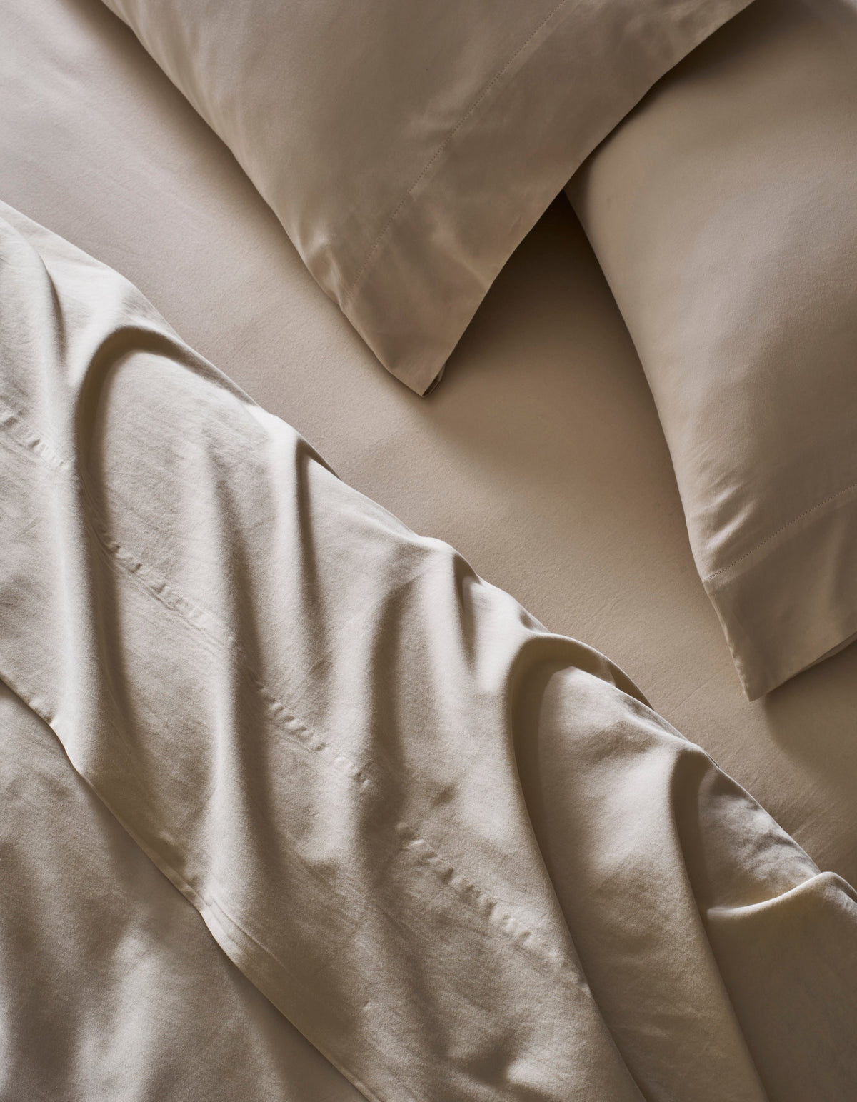 A close-up of a neatly made bed with Cozy Earth’s Soft-Wash Cotton Bedding Core Bundle, featuring beige sheets, matching pillowcases, and a slightly rumpled flat sheet over the fitted sheet and pillows.|Color:Driftwood