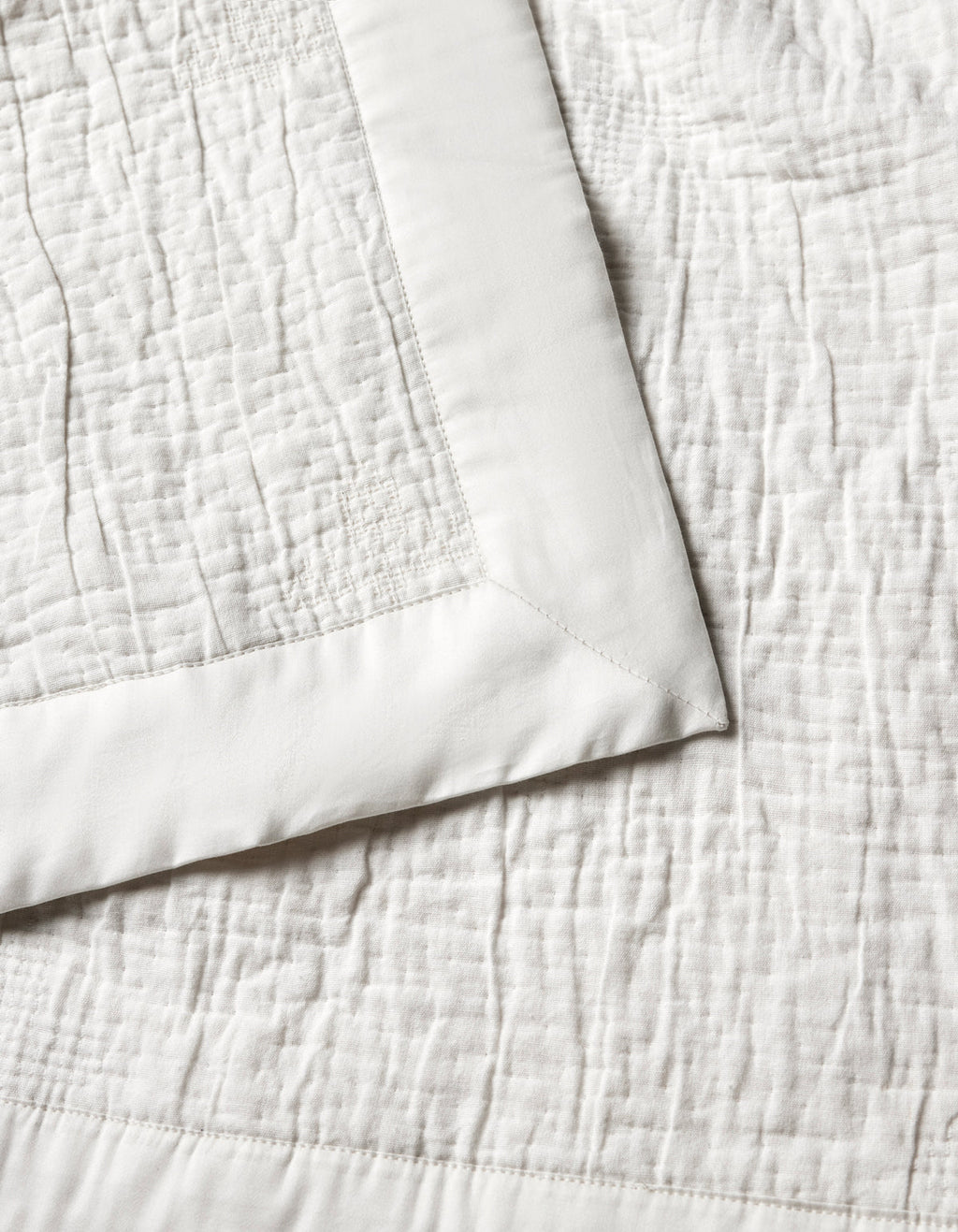 The Cozy Earth Little Bee Matelasse Baby Blanket features a cream hue, textured stitched pattern, and smooth solid border. A folded corner highlights both the elegant surface and refined edging.|Color:Sea Salt