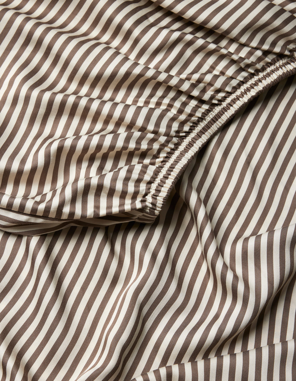 Close-up of Cozy Earth Bamboo Fitted Sheet, showcasing brown and white vertical stripes with a gathered, elasticized section and a smooth, flowing texture.|Color:Classic Stripe in Ebony