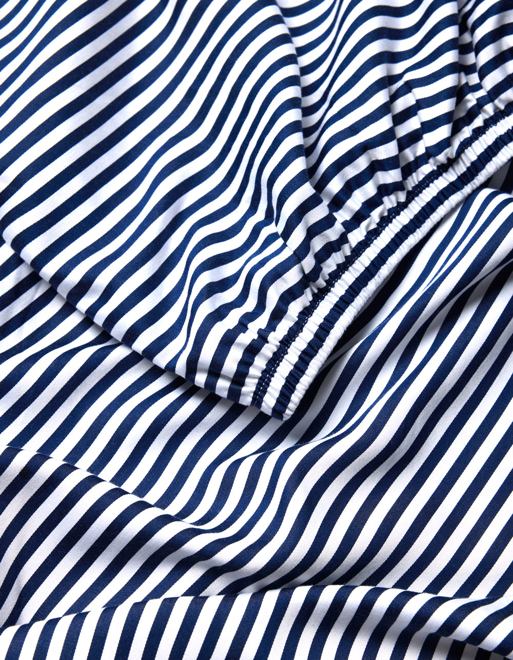 A close-up of the Cozy Earth Bamboo Fitted Sheet shows its navy blue and white stripes, with elasticized sections that gather the fabric into soft folds and curves.|Color:Classic Stripe in Pacific