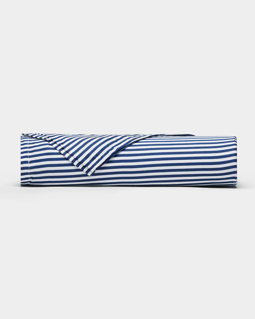 A Bamboo Sheet Set by Cozy Earth in navy blue and white stripes lies rolled on a plain white surface, with one corner partially unfolded to reveal the underside of the fabric.|Color:Classic Stripe in Pacific