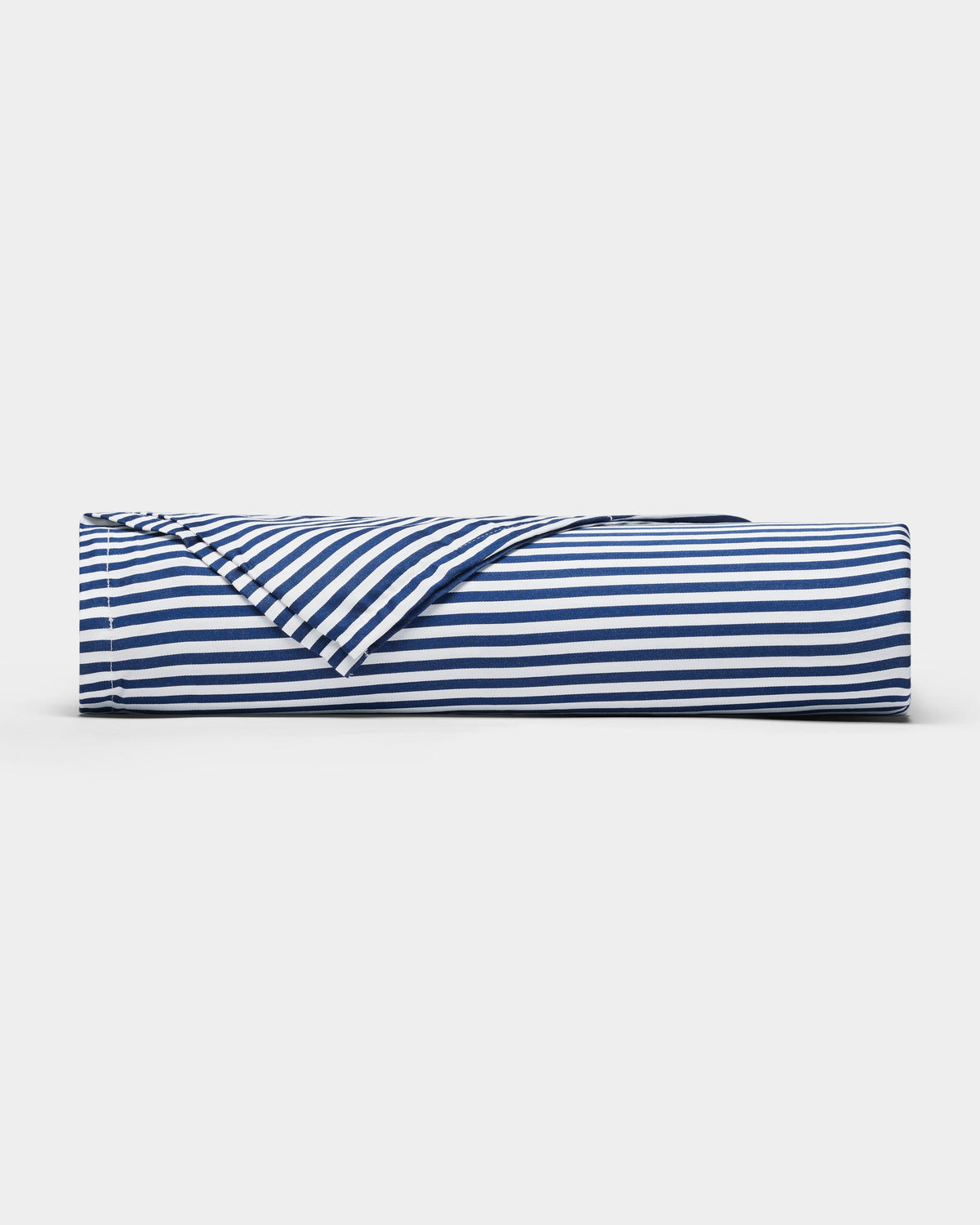 A Bamboo Sheet Set by Cozy Earth in navy blue and white stripes lies rolled on a plain white surface, with one corner partially unfolded to reveal the underside of the fabric.|Color:Classic Stripe in Pacific