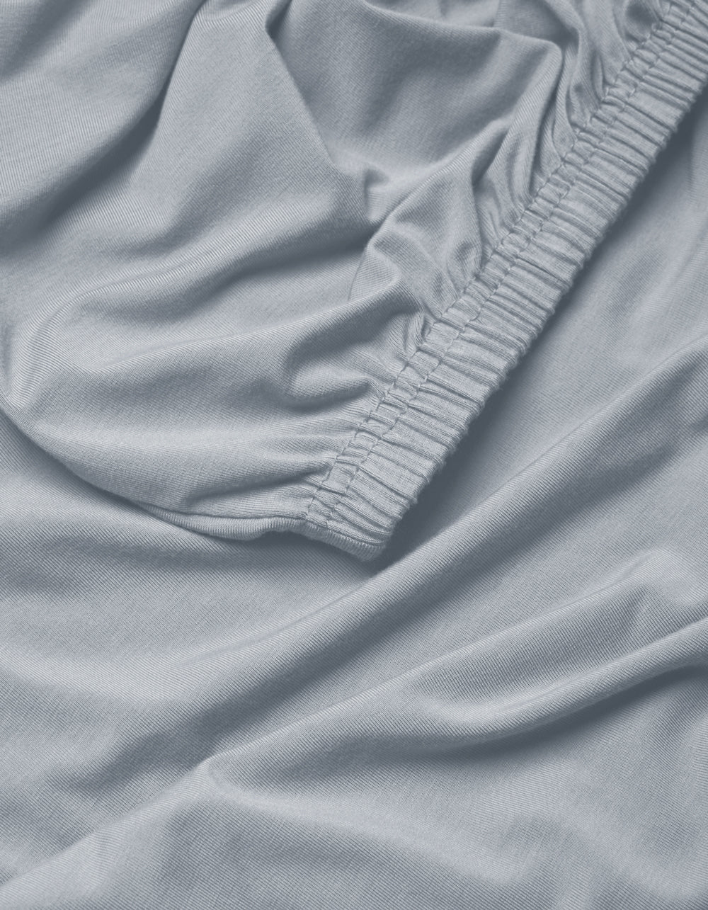 Close-up of Cozy Earth's Bamboo Jersey Fitted Sheet in light blue, featuring gathered elastic edges and a soft, slightly wrinkled fabric texture.|Color:Shore