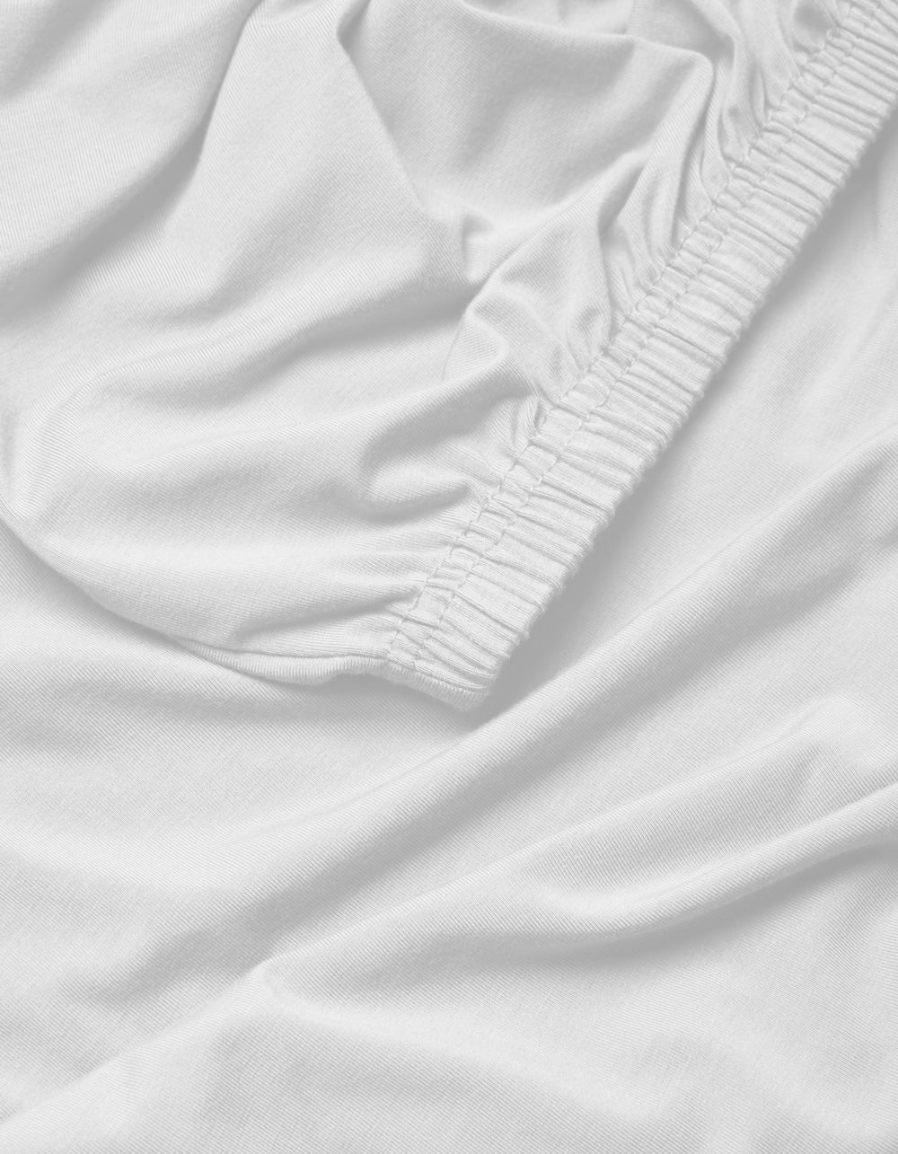A close-up of the Cozy Earth Bamboo Jersey Fitted Sheet highlights its elasticized edge, smooth surface, and gentle folds for a soft, snug fit.|Color:White