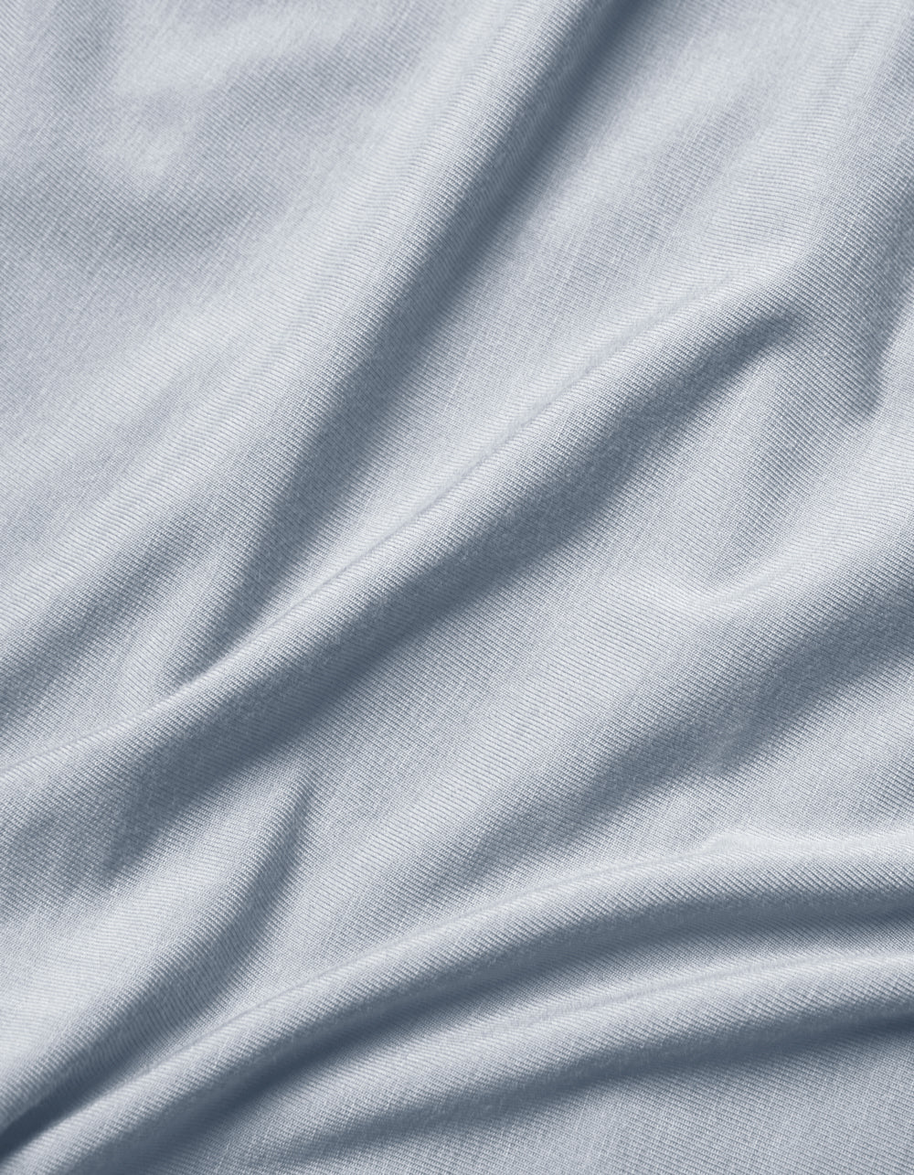 Close-up of Cozy Earth Bamboo Jersey Flat Sheet in light grey or pale blue, featuring soft folds, subtle texture, and gentle shadows and highlights.|Color:Shore