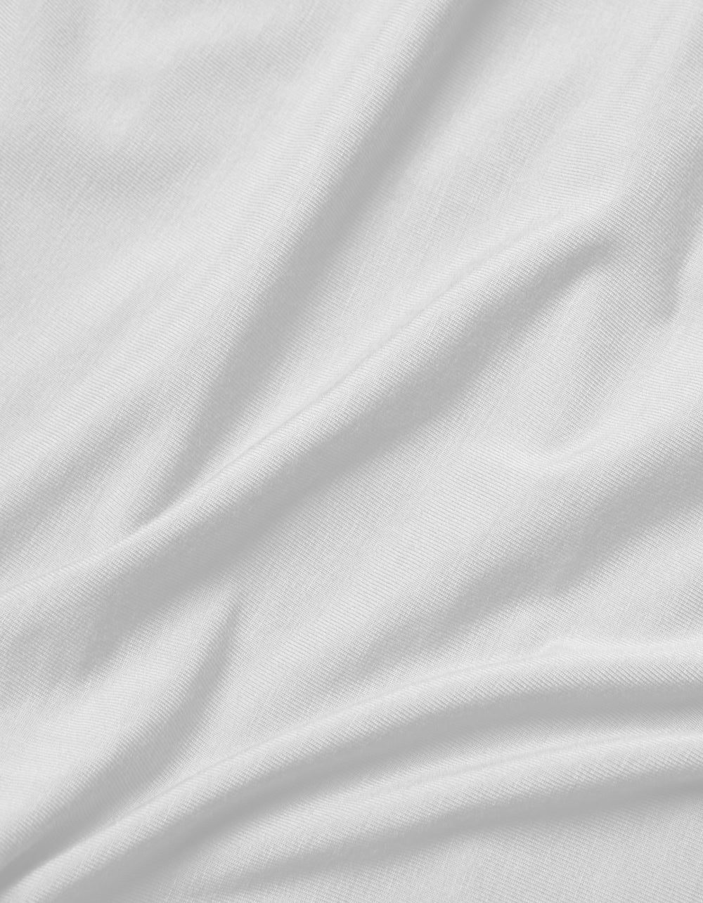 A close-up of the Cozy Earth Bamboo Jersey Flat Sheet shows its smooth white fabric with soft folds, gentle creases, and subtle shadows, highlighting the luxurious texture.|Color:White