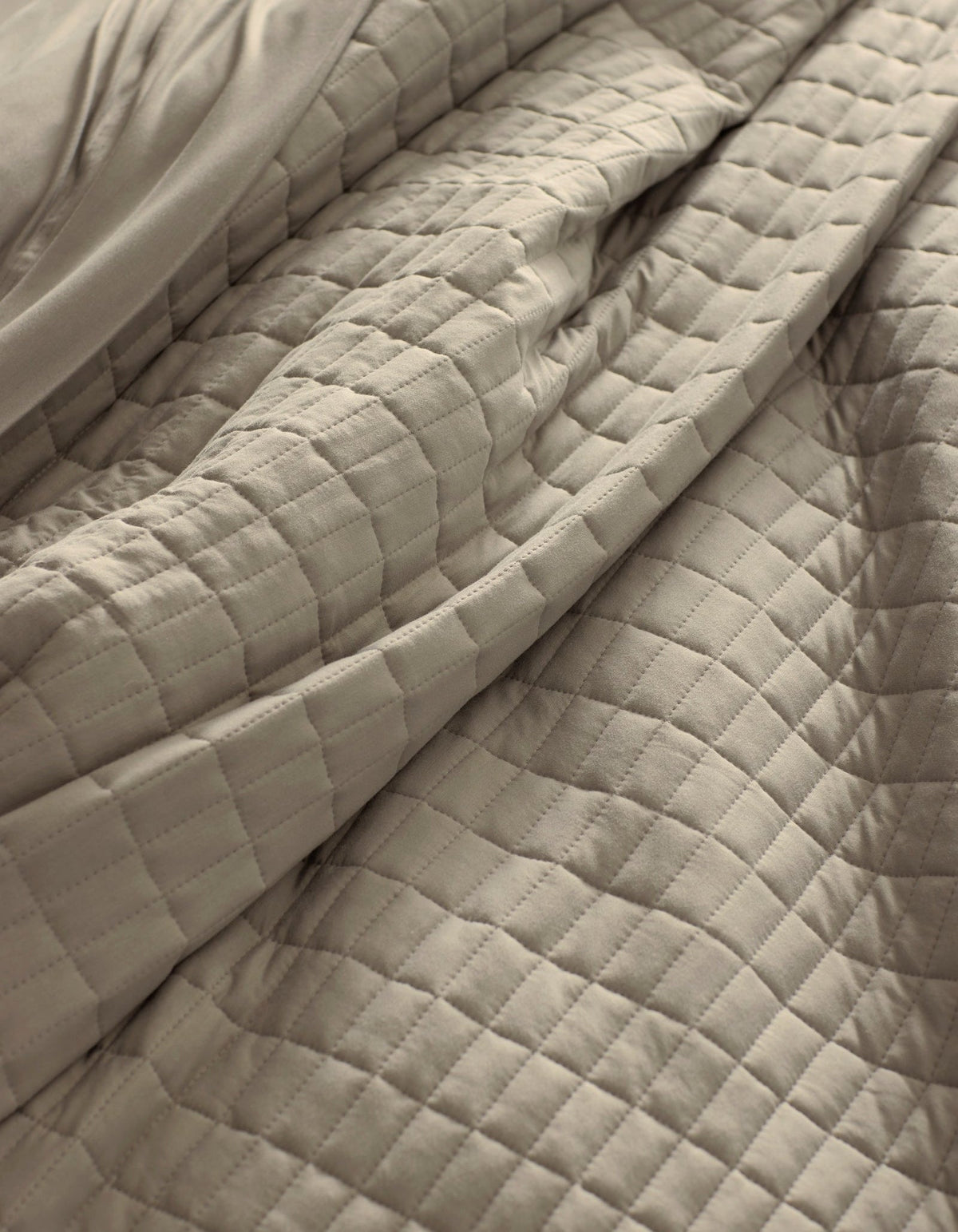 A close-up of the Cozy Earth Bamboo Jersey Quilt in beige, featuring a soft, quilted square pattern with gentle folds and visible texture.|Color:Driftwood