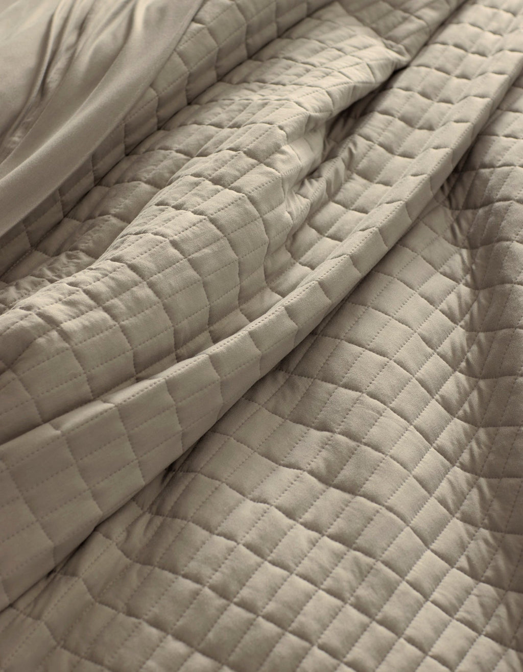 A close-up of the Cozy Earth Bamboo Jersey Quilt in beige, featuring a soft, quilted square pattern with gentle folds and visible texture.|Color:Driftwood